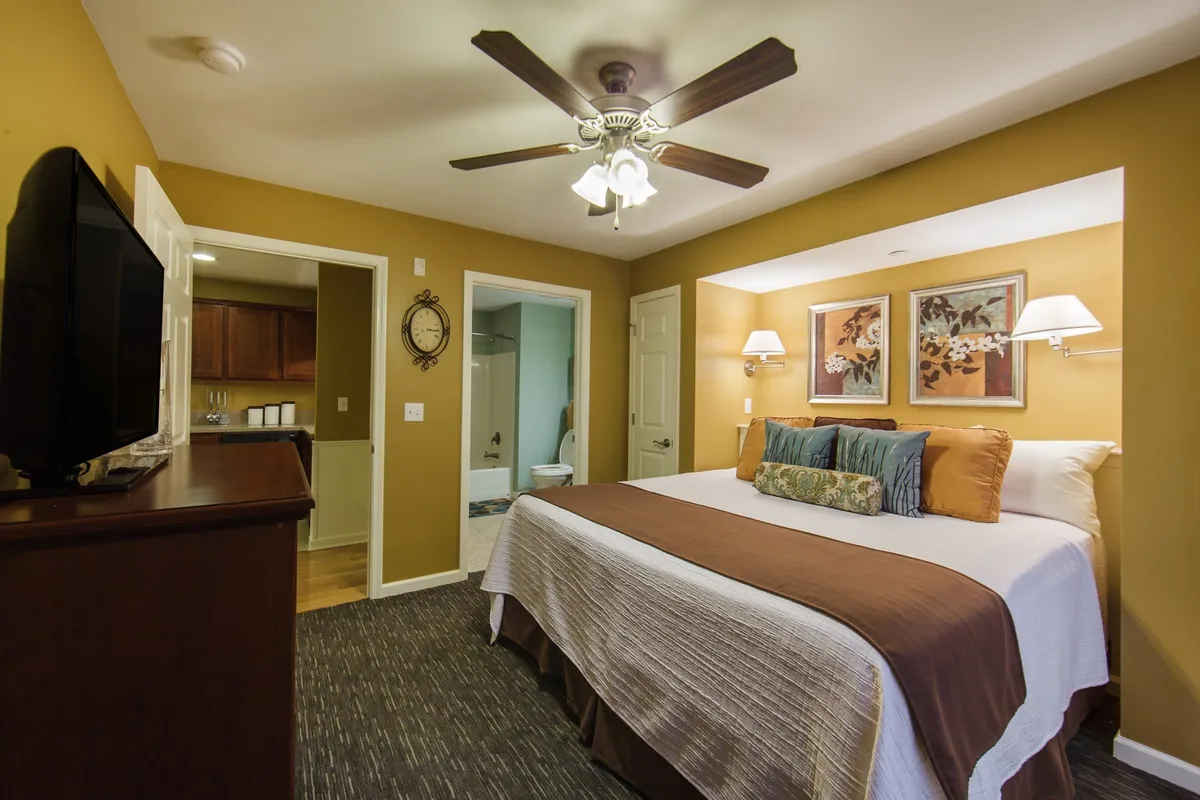 This image presents a serene bedroom featuring a plush king bed adorned with crisp linens, matching nightstands with soft lighting, a large TV set for entertainment, and tasteful wall artwork. The cozy atmosphere is inviting, evoking restful nights and relaxing mornings.