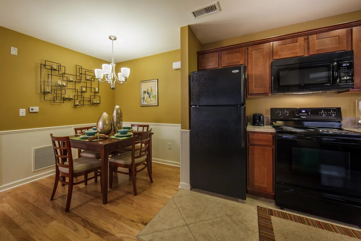 Showcasing a warm, open-plan interior with a dining table under a chandelier, modern kitchen appliances in the background, and elegant wall art, this image captures the heart of the villa's social spaces. The setting is perfect for shared meals, casual entertaining, and memorable family gatherings.