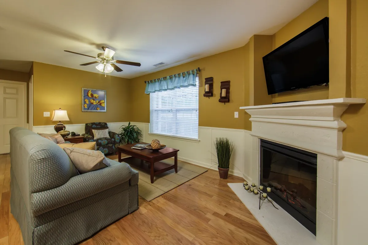 This inviting interior scene showcases a plush, comfortable sofa facing a glowing fireplace, with a stylish coffee table and a large television nearby. Tasteful artwork adorns the walls, creating a warm, welcoming space perfect for relaxing, socializing, or unwinding after a day on the golf course or exploring Branson.