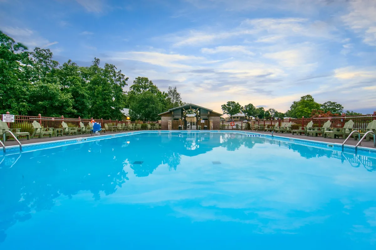 A vibrant outdoor swimming pool scene set amidst lush greenery, with poolside chairs and a cabana creating a welcoming atmosphere. Guests are seen swimming, basking in the sun, and socializing, while the golden hour lighting adds to the relaxed resort vibe.